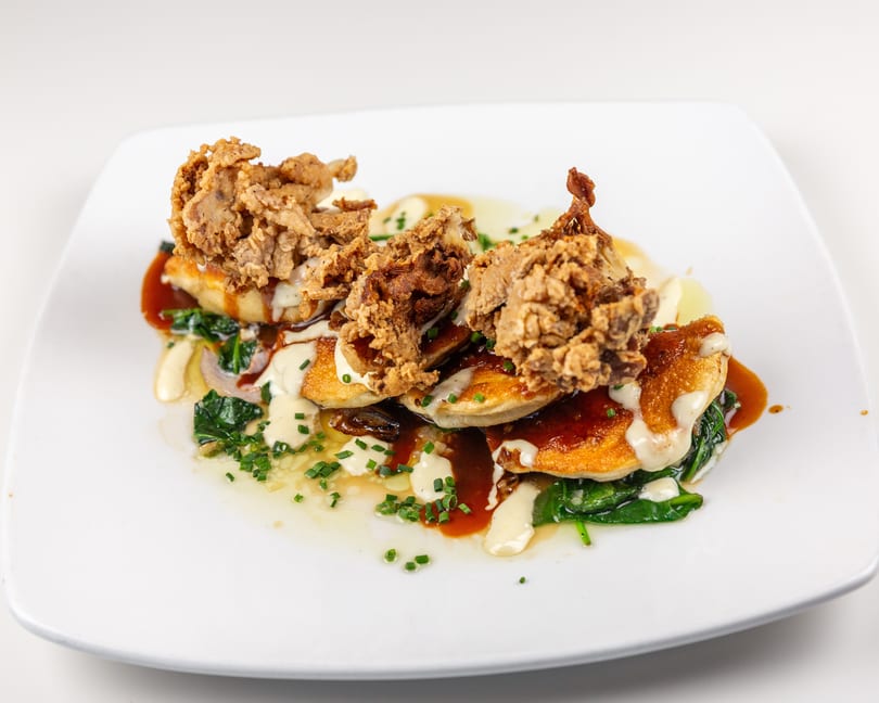 Crispy fried mushrooms on golden pancakes with spinach, rich sauces, and fresh chives.