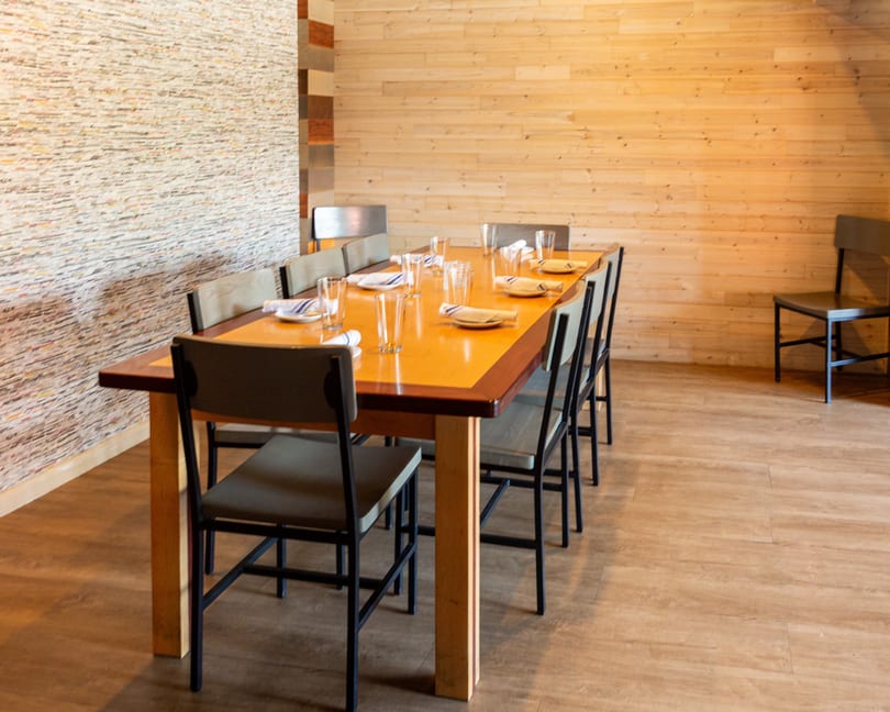Set wooden dining table with chairs in a restaurant featuring textured and wood-paneled walls.