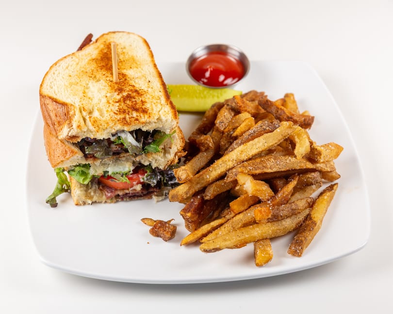 Toasted sandwich with lettuce, tomato, bacon, and seasoned fries, served with a pickle and ketchup.