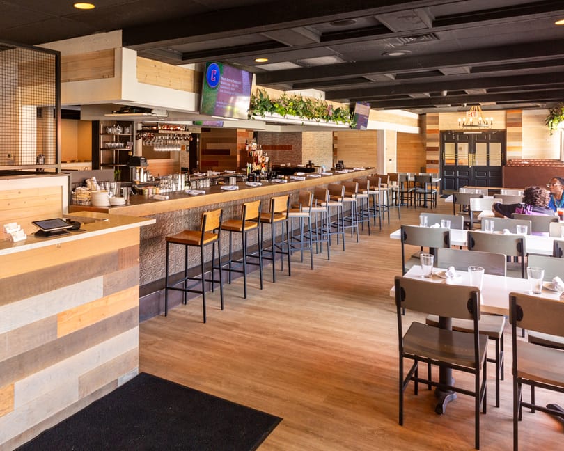 FORAGE restaurant interior with a long bar, dining tables, wood accents, and TV screens showing sports.