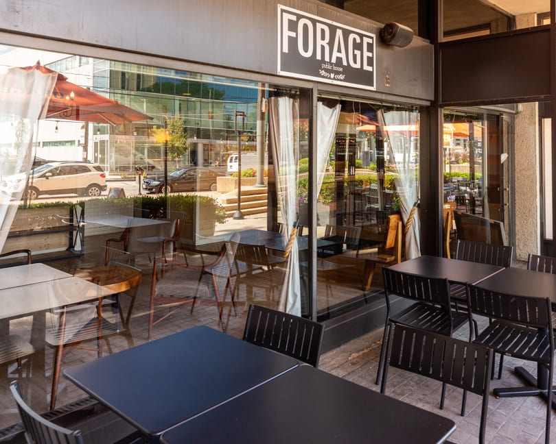 Forage Public House & Cafe sign above an outdoor patio with black tables and chairs.